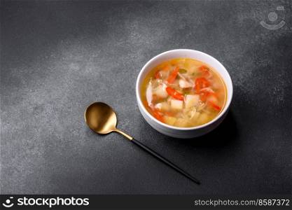 Chicken soup with noodles and vegetables in bowl over rustic concrete background. Homemade healthy meal. Closeup of a bowl of chicken noodle and vegetable soup on a concrete table