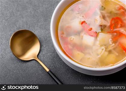 Chicken soup with noodles and vegetables in bowl over rustic concrete background. Homemade healthy meal. Closeup of a bowl of chicken noodle and vegetable soup on a concrete table