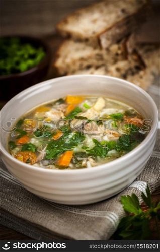 Chicken soup with rice and vegetables. Chicken rice soup with vegetables in bowl and bread on rustic table