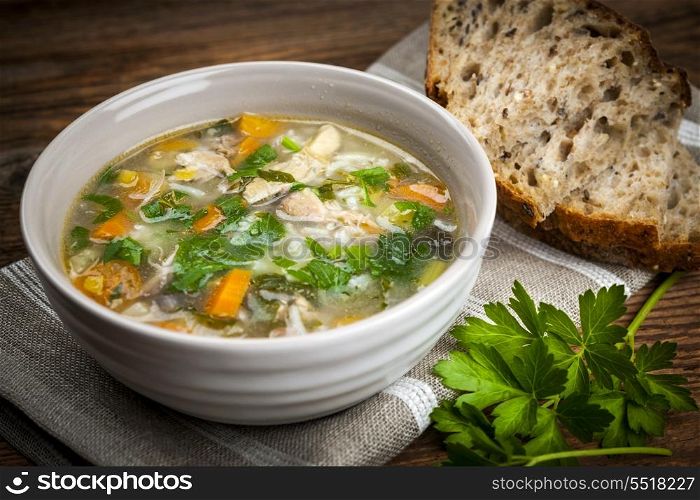Chicken soup with rice and vegetables. Chicken rice soup with vegetables in bowl and bread on rustic table
