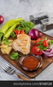Chicken steak placed on a wooden tray with bell peppers, tomatoes, red onions, pineapple sauce, lettuce, and sesame seeds