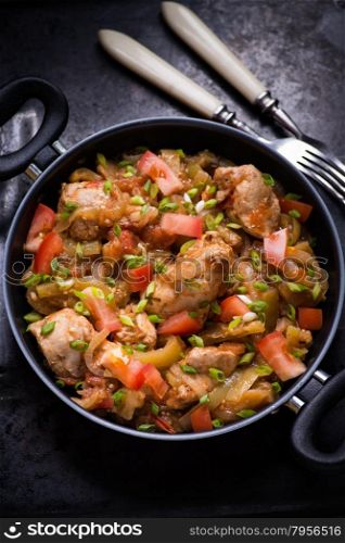Chicken stew with onion, pepper ant tomato, selective focus, dark background, top view