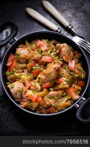 Chicken stew with onion, pepper ant tomato, selective focus, dark background, top view