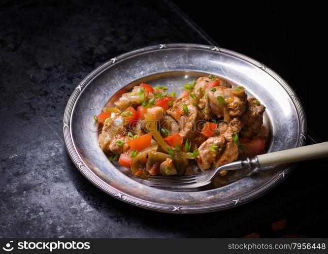 Chicken stew with onion, pepper ant tomato, vintage plate, selective focus, dark background