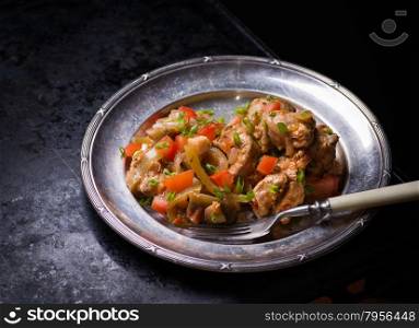 Chicken stew with onion, pepper ant tomato, vintage plate, selective focus, dark background