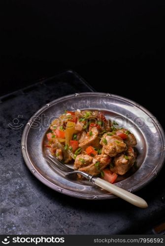 Chicken stew with onion, pepper ant tomato, vintage plate, selective focus, dark background