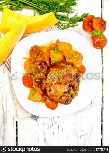 Chicken stew with pumpkin, dried apricots, carrots and red wine, sprinkled with sesame seeds in a plate on a napkin against wooden board on top