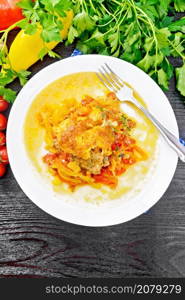 Chicken stewed with tomatoes, yellow and red bell peppers and cheese in white plate on a napkin, thyme, parsley and garlic on black wooden board background from above