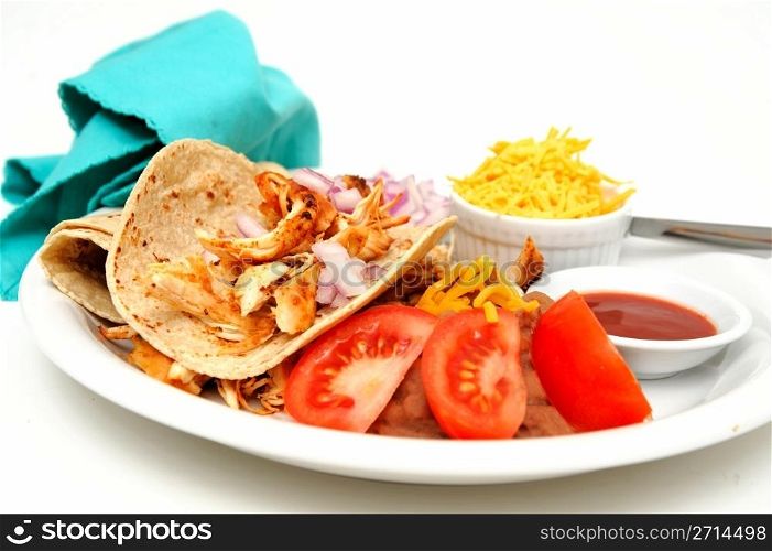 Chicken Taco. Shredded grilled spiced chicken on a white plate with fresh tortilla&rsquo;s, refried beans with sides of red onion, cheddar cheese and hot sauce.