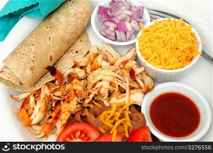 Chicken Tacos And Refried Beans. Shredded grilled spiced chicken on a white plate with fresh tortilla&rsquo;s, refried beans with sides of red onion, cheddar cheese and hot sauce.