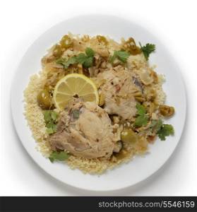 Chicken thighs cooked with olives, onions and orange and lemon juice, served over a bed of couscous and garnished with coriander (cilantro) leaves, viewed from above