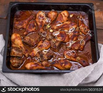 chicken thighs in tomato honey sauce on a black baking sheet, close up. chicken thighs in tomato honey sauce