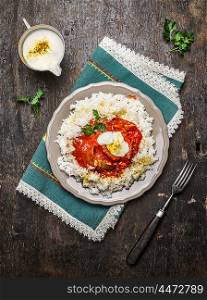 Chicken tomato stew with basmati rice with yoghurt sauce in plate and fork on wooden background, top view