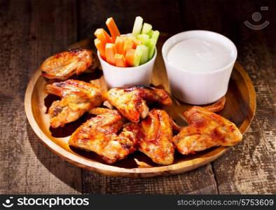 chicken wings with fresh vegetables and sauce on wooden table