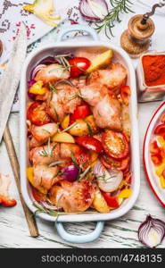 Chicken with colorful vegetables and red paprika powder in casserole, bake preparation on light rustic kitchen table , top view