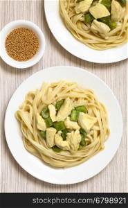Chicken with green bell pepper and onion in mustard cream sauce on fettuccine pasta served on plates, raw mustard seeds in small bowl on the side, photographed overhead with natural light