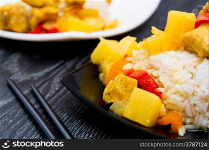 chicken with pineapple and garnished with rice on white and black plates.