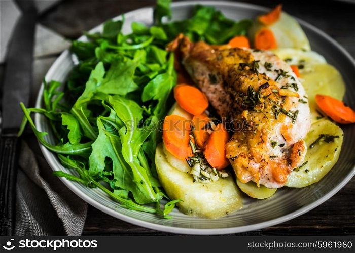 Chicken with potatoes and arugula salad on rustic background