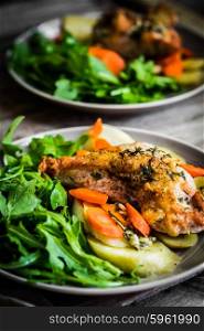 Chicken with potatoes and arugula salad on rustic background