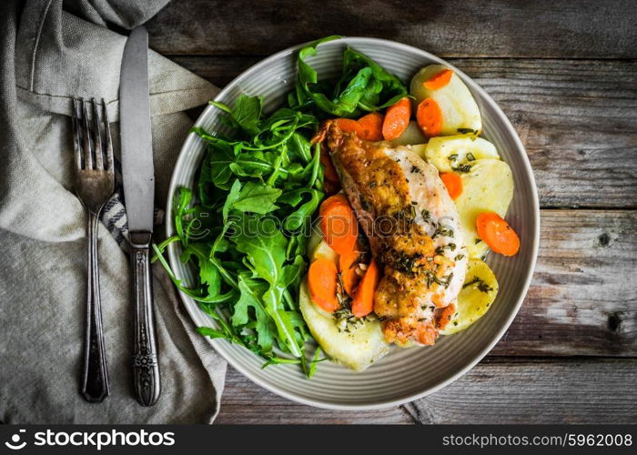 Chicken with potatoes and arugula salad on rustic background