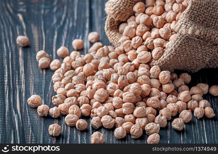 Chickpea spill out of the bag closeup on wooden background. Bag with chickpeas on table closeup