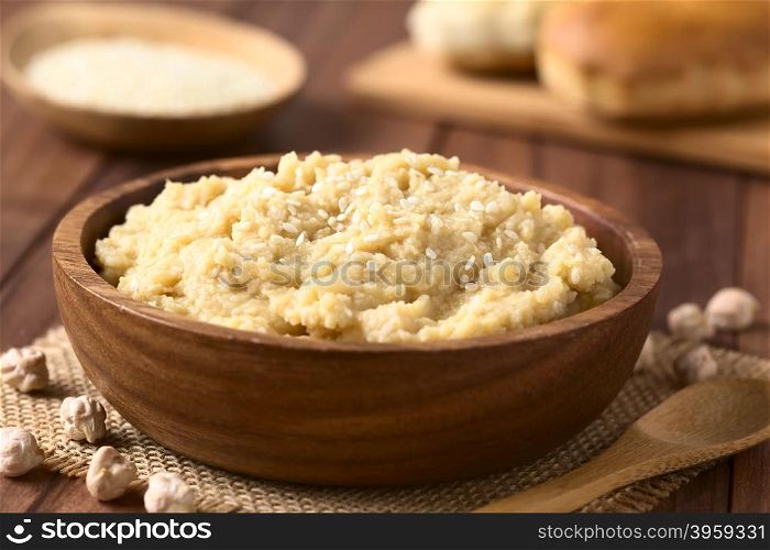 Chickpea spread or hummus with sesame seeds in wooden bowl, photographed with natural light (Selective Focus, Focus one third into the chickpea spread)