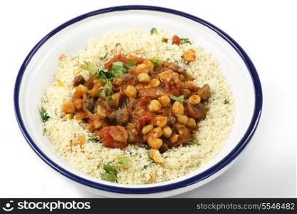 Chickpeas or garbanzo beans and quartered button mushrooms cooked in a spicy tomato and onion sauce and served with couscous mixed with parsley and refreshed dried apricots, Moroccan style, served in a tagine bowl
