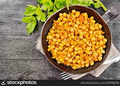 Chickpeas stewed with celery, tomatoes, onions, carrots and garlic in a frying pan on sackcloth on a background of dark wooden board from above