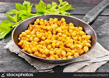 Chickpeas stewed with celery, tomatoes, onions, carrots and garlic in a pan on sackcloth on dark wooden board background