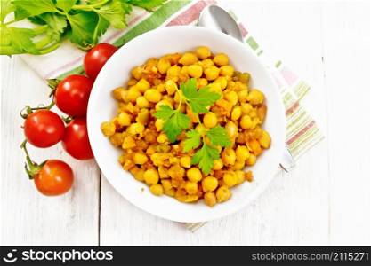 Chickpeas stewed with celery, tomatoes, onions, carrots and garlic in a plate on a napkin on wooden board background from above