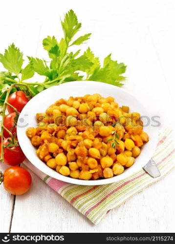 Chickpeas stewed with celery, tomatoes, onions, carrots and garlic in a plate on a towel on white wooden board background