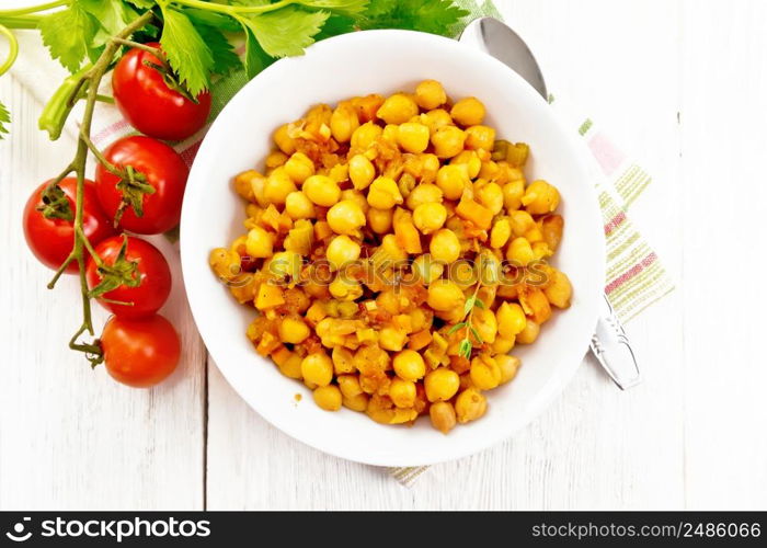 Chickpeas stewed with celery, tomatoes, onions, carrots and garlic in a plate on a towel on wooden board background from above