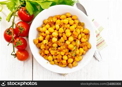 Chickpeas stewed with celery, tomatoes, onions, carrots and garlic in a plate on a towel on wooden board background from above