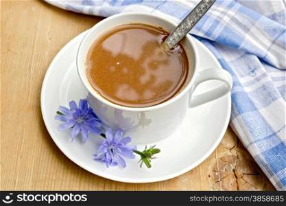 Chicory drink in a white cup with a flower and a spoon, napkin on a wooden boards background