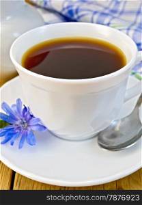 Chicory drink in a white cup with a flower on a saucer and spoon, napkin, milk jug on a wooden boards background