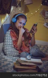 child and gadget addiction. girl in headphones in the childrens room lies on the bed and looks at the phone
