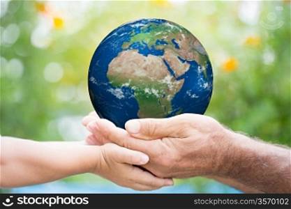 Child and senior man holding planet Earth in hands against green spring background. Elements of this image furnished by NASA