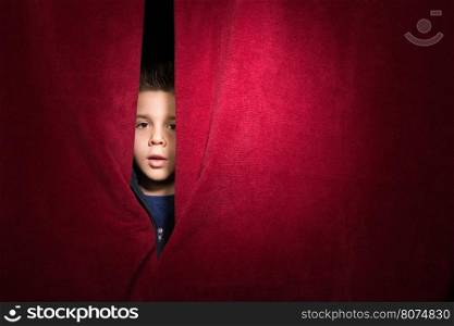 Child appearing beneath the curtain. Red curtain.