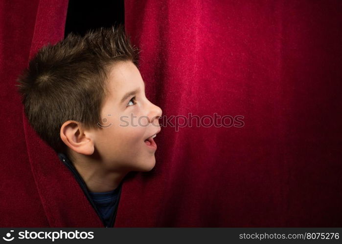 Child appearing beneath the curtain. Red curtain.