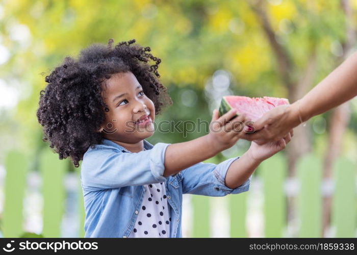 Child black girl happy with a slice of watermelon receiving from her mother. Summer concept