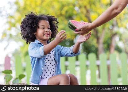 Child black girl happy with a slice of watermelon receiving from her mother. Summer concept