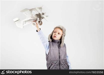 Child boy playing with paper toy airplane and dreaming of becoming a pilot against a white background