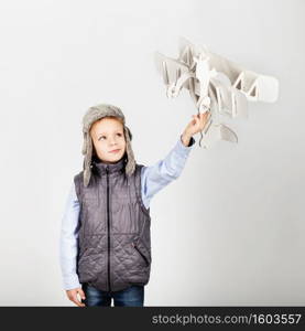 Child boy playing with paper toy airplane and dreaming of becoming a pilot against a white background