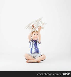 Child boy playing with paper toy airplane sitting on the floor against a white background. Kid dreaming of becoming a pilot. Childhood. Fantasy, imagination.