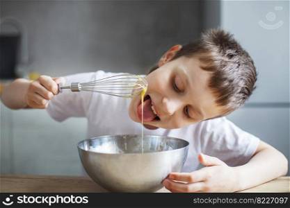 Child cooking at the kitchen. boy stirring dough for a cake in the steel bowl. the kid tastes food and licks a whisk. Child cooking at the kitchen. boy stirring dough for a cake in the steel bowl. kid tastes food and licks a whisk