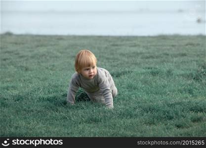 child creeps on the grass at seashore, autumn outdoor