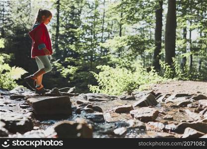 Child crossing mountain stream. Little girl walking in mountains, spending summer vacation close to nature