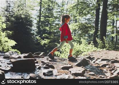 Child crossing mountain stream. Little girl walking in mountains, spending summer vacation close to nature