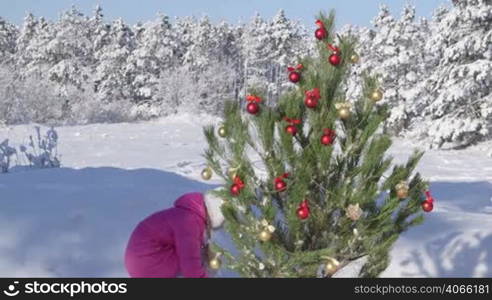 Child decorating Christmas tree in snow covered winter forest