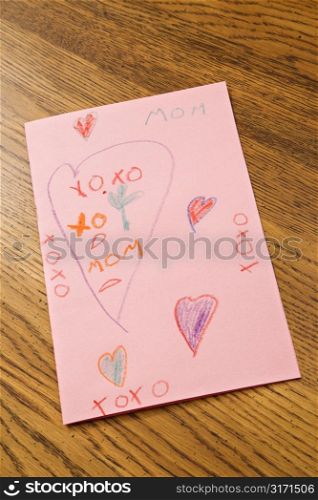 Child drawing with crayons on pink paper.
